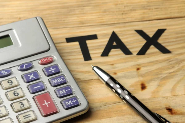 The word tax of paper letters and a calculator and pen on a natural wooden table. Taxes