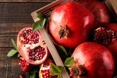 Kahverengi ahşap bir masa üzerinde ahşap bir kutu içinde yaprakları ile olgun lezzetli kırmızı nar meyve. üst görünüm