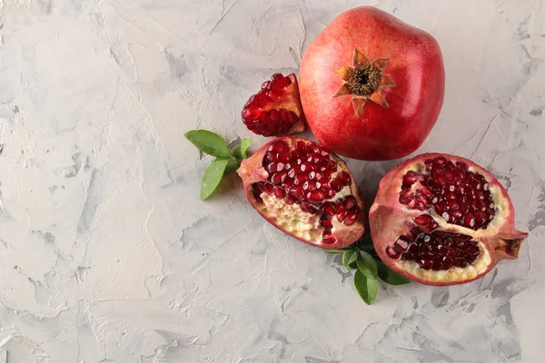 Olgun lezzetli kırmızı nar meyve ve hafif beton arka plan üzerinde yaprakları ile nar parçaları. üst görünüm