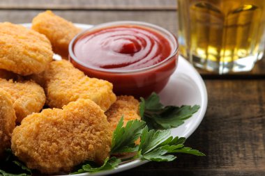 Kırmızı soslu tavuk külçeleri ve kahverengi ahşap bir masada bira. fast food. Close