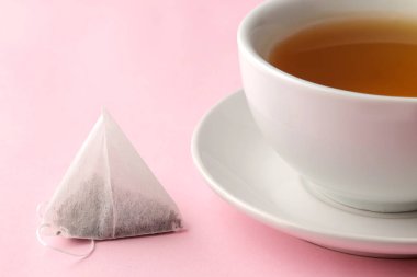 Çay poşeti piramit ve hassas pembe arka plan üzerinde çay ile fincan. çay yapmak için.