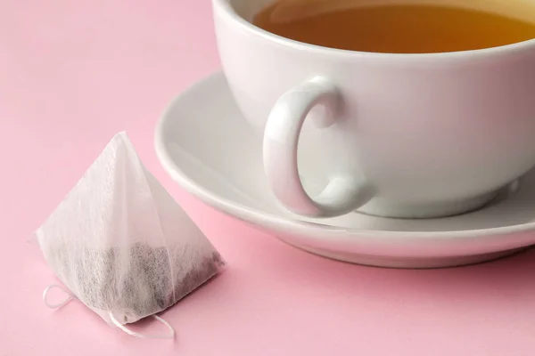 繊細なピンクの背景にティーバッグピラミッドと紅茶とカップ お茶を作る — ストック写真