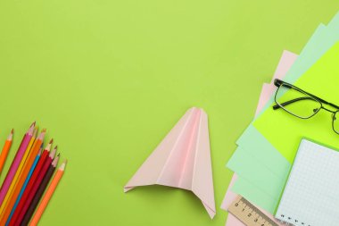 Okula geri dön. kırtasiye, okul malzemeleri gözlük, renkli kalem ve parlak yeşil arka plan üzerinde bir kağıt düzlem. üst görünüm