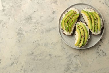 Hafif beton arka plan üzerinde bir tabak üzerinde ekmek ve avokado dilimleri bir sandviç. Sandviç yapıyorum. üst görünüm