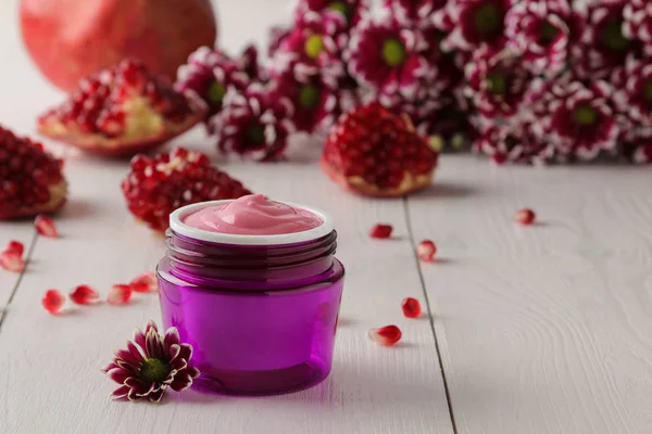 Cream. cosmetics for face and body. Pink cream and flower in a purple jar on a white wooden table.