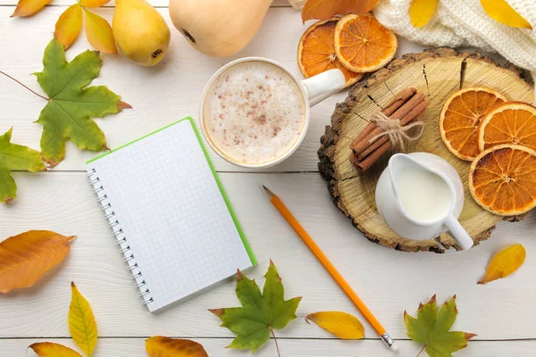Hot autumn drink, coffee or cocoa, with a notebook, yellow leaves and decorative pumpkins on a white wooden table. autumn composition. top view.