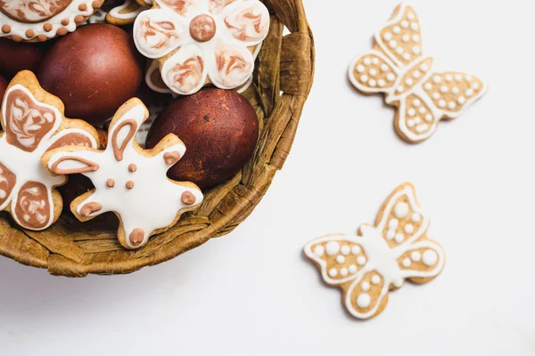 Gingerbread çerezleri bir Paskalya tavşanı, çiçekler ve kelebekler, şeklinde çikolata ve Beyaz pudra şekeri ve yumurta beyaz bir yüzey üzerinde kahverengi bir sepet içinde kaplı