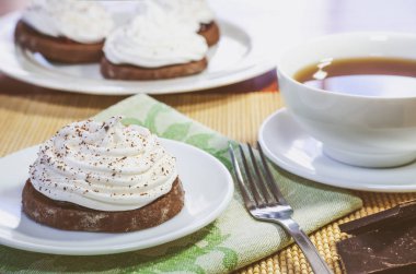 Yumurta beyaz krem ile çikolatalı kek, bir fincan çay, çikolata parçaları ve ahşap bir masa üzerinde bir çatalı
