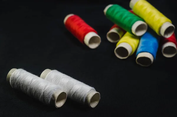 Spools of green, blue, red, yellow and white threads on black fabric