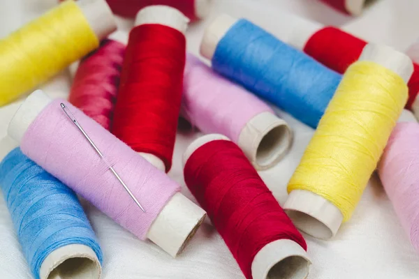Makaralar, pembe, sarı, mavi ve kırmızı konu ve beyaz pamuklu kumaş üzerine dikiş iğnesi
