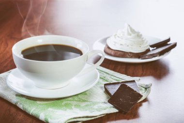 Bir fincan sıcak kahve, çikolata parçaları ve yumurta akı woodeb masaya krem bir çikolatalı kek