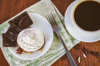 Yumurta beyazı krema, çikolata, anason, kakule ve yeşil bir peçete üzerinde çatalı adet ve ahşap bir masa üzerinde sıcak kahve ile bir pasta