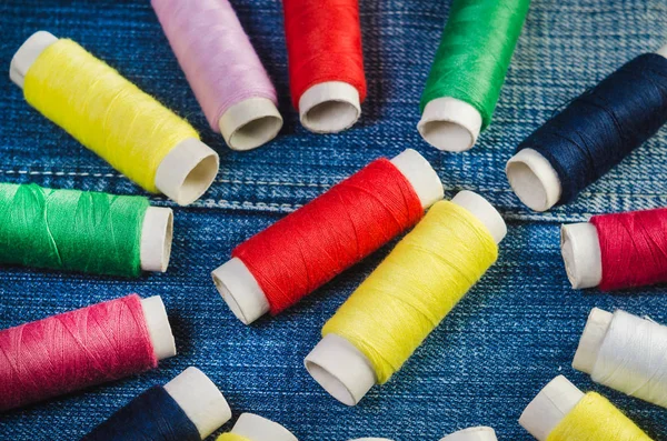 A circle of colored thread spools with a center of red and yellow thread spools on a denim