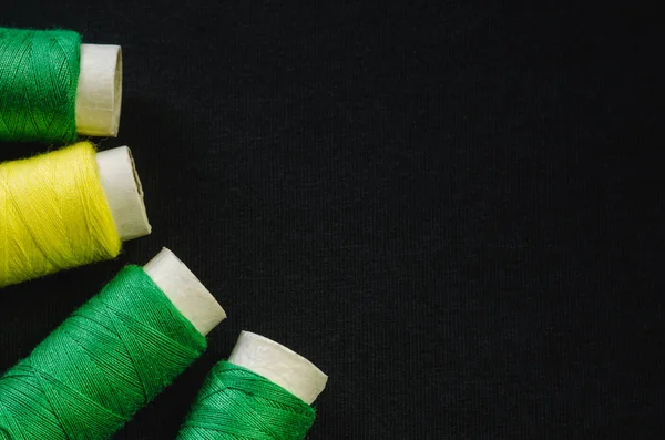 Spools of green and yellow thread on black fabric