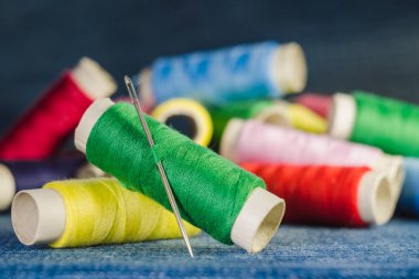 Biriktiricileri denim kumaş üzerinde renkli iş parçacığı arka plan üzerinde bir iğne ile yeşil iplik makarası