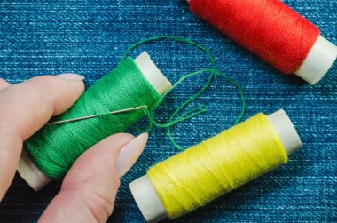 Bir kot arka planda biriktiricileri kırmızı ve sarı iş parçacığı ile el parmakları bulunan yeşil iş parçacığı biriktirme