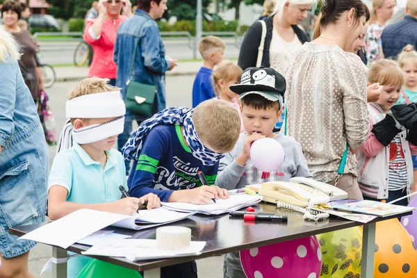 İki küçük blindfolded çocuklar kağıt üzerinde bir tablo çizmek ve küçük bir çocuk bir kalabalık içinde bir yaz gününde bir balon açılırsa.
