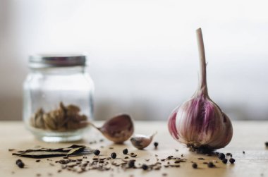 Baş sarımsak, karabiber, kimyon tohumu, defne yaprakları ve baharat hafif ahşap bir masa üzerinde bir kavanoz