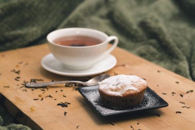 Bir ahşap tepsi yeşil tekstil bir arka plan üzerinde doğal katkı maddeleri ile pudra şekeri bir siyah plaka ve beyaz bir bardak çay ile ev yapımı kek. Yatakta rahat kahvaltı kavramı