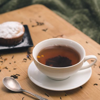 Bir ahşap tepsi yeşil tekstil bir arka plan üzerinde doğal katkı maddeleri ile pudra şekeri bir siyah plaka ve beyaz bir bardak çay ile ev yapımı kek. Yatakta rahat kahvaltı kavramı