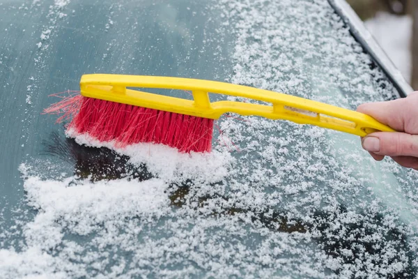 The process of cleaning the windshield of the car from the snow with a red and yellow brush
