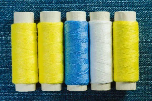 在粗斜纹棉布上排成一排的白色 黄色和绿色缝纫线的线轴 — 图库照片