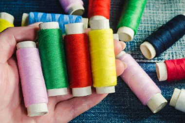 Bir el denim iş parçacığında başka biriktiricileri arka planı yeşil, kırmızı, pembe ve sarı dikiş iplik makarası