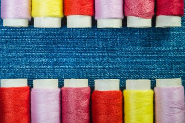 Mavi kot üzerinde iki sıra halinde kopya alanı ile yerleştirilmiş renkli dikiş ipliği makaralar