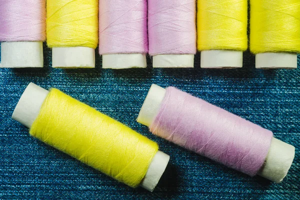 蓝色粗斜纹棉布上的粉红色和黄色缝纫线的线轴 — 图库照片