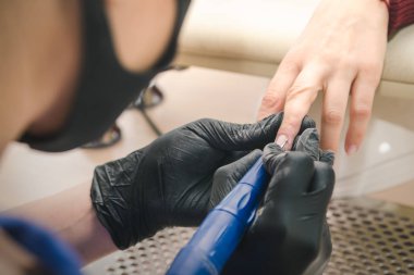 Siyah lateks eldiven bir manikürcü bir donanım yapar bir güzellik salonu bir el ile elektrikli freze makinesi kullanan bir istemci için manikür.