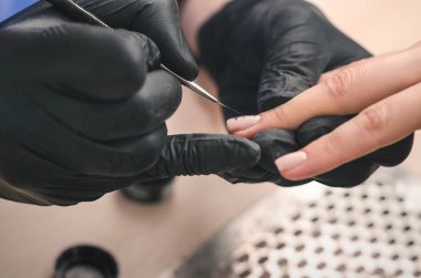 Siyah lateks eldiven bir manikürcü istemcinin çivi ile bir güzellik salonu bir jel Lehçe üzerinde bir desen uygular, yakın çekim.