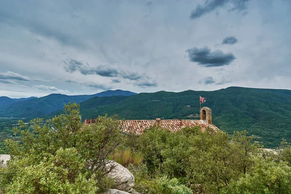 Amer, İspanya dağlarla çevrili bazı ağaçların arkasında görülen bir kilise çatısı
