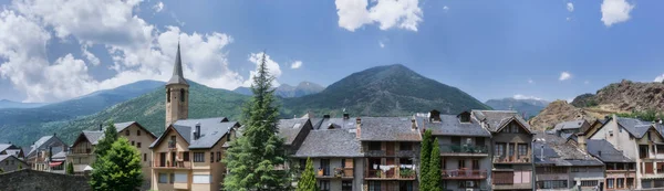 Panoramic view of a pyrenean village,s homes & bell tower in front of the mountains & a slightly cloudy sky Panoramic view of a pyrenean village in front of the mountains