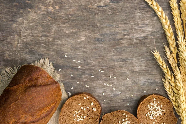 Homemade brown black on wooden background, black bread with rye spike and sesame, country still life top view