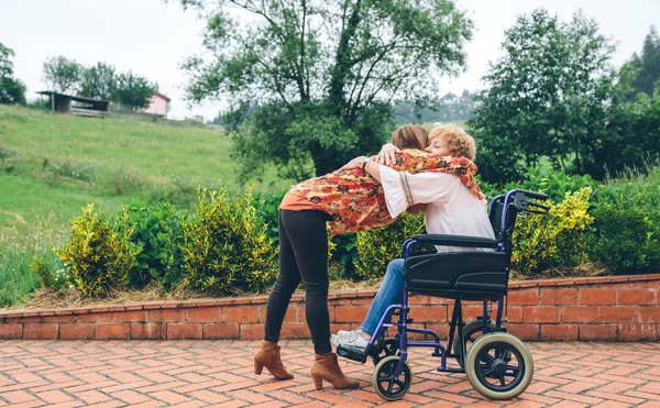 Дочь обнимает свою старшую мать в инвалидном кресле — стоковое фото