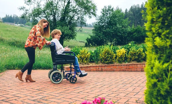 Mulher carregando sua mãe em uma cadeira de rodas — Fotografia de Stock