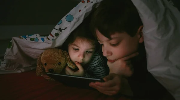 Bröderna tittar på tabletten i mörkret — Stockfoto