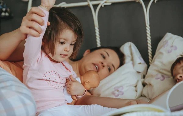 Bebê menina leitura livro com a família na cama — Fotografia de Stock