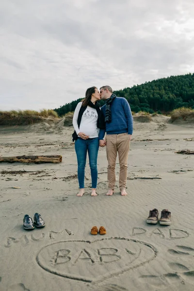 Mamma, Pappa och baby skrivet på sanden med föräldrarna kyssar bakom — Stockfoto