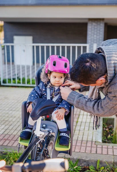 Padre cerrando el casco a su hija sentada en el asiento de la bicicleta —  Fotos de Stock