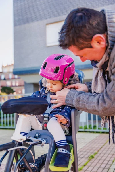 Padre cerrando el casco a su hija sentada en el asiento de la bicicleta — Foto de Stock