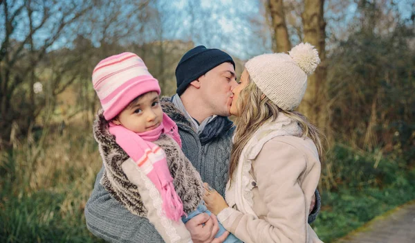 Pareja feliz con hija besándose en el bosque — Foto de Stock