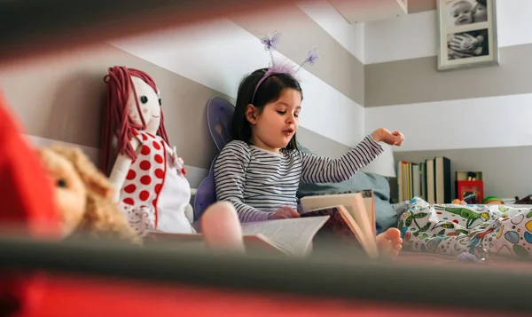 Menina disfarçada lendo um livro para sua boneca — Fotografia de Stock