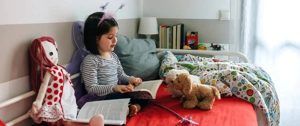 Menina disfarçada lendo um livro para seus brinquedos — Fotografia de Stock