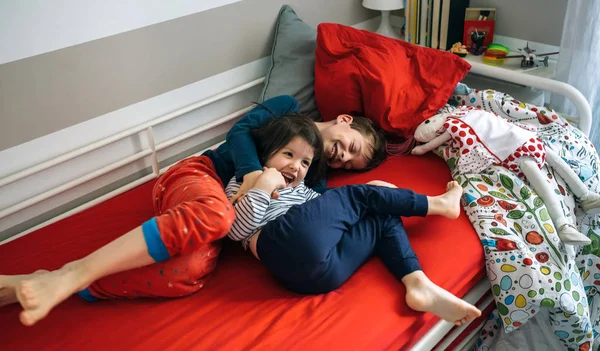 Hermanos haciendo cosquillas y riendo acostados en la cama —  Fotos de Stock