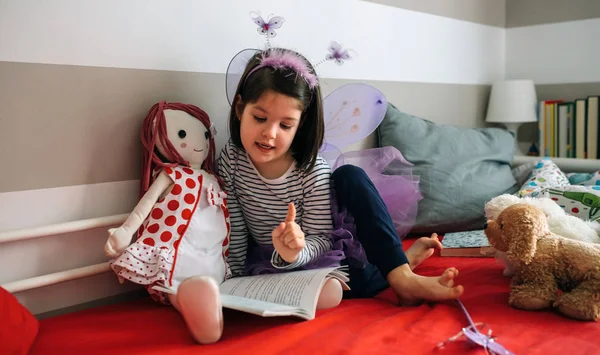 Girl disguised reading a book to her doll — Stock Photo, Image