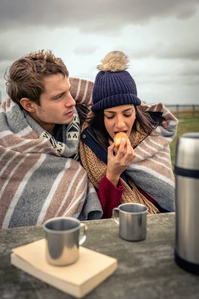 Giovane coppia sotto coperta mangiare muffin all'aperto in una giornata fredda — Foto Stock