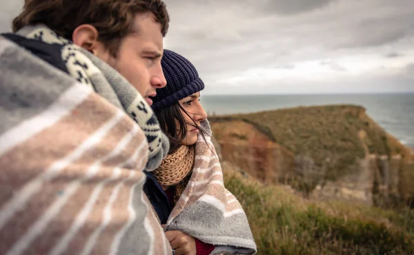 Young couple under blanket looking the sea in a cold day — Stock Photo, Image