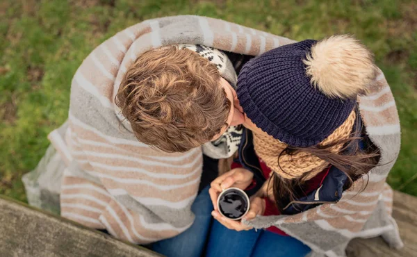 Pareja joven bajo manta con bebida caliente besándose al aire libre —  Fotos de Stock