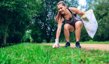 Plogging açık havada yapıyor çöp torbası ile çömelme kız